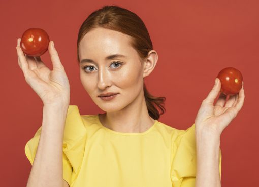 Kobieta trzymająca dwa pomidory na czerwonym tle, symbolizujące naturalne źródło likopenu – składnika popularnych suplementów diety.